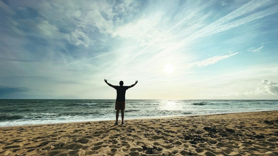 Person with arms raised on beach at sunset