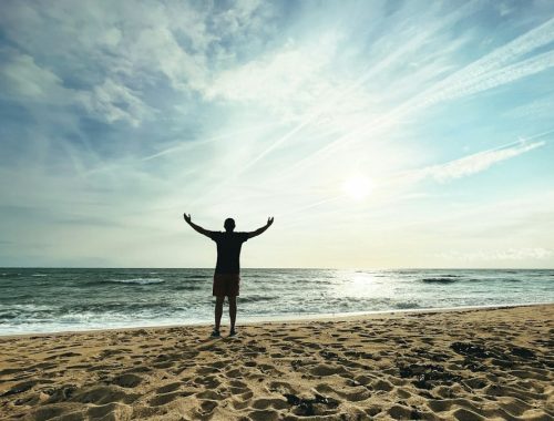 Person with arms raised on beach at sunset