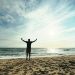 Person with arms raised on beach at sunset